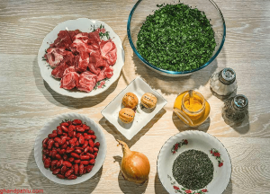 تصویر مواد اولیه قورمه سبزی شامل سبزی خشک، گوشت خورشتی، پیاز، لوبیا قرمز، لیمو عمانی و ادویهها